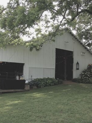 White barn with open doors beside a grassy lawn and overhanging tree branches