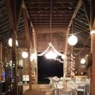 Dimly lit rustic restaurant with wooden beams, hanging lights, and white-clothed tables set for dining