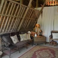 Rustic cabin sitting area with woven sofa, side table, lamp, and patterned rug under slanted wooden beams