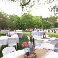 Outdoor banquet tables with white chairs and pink floral centerpieces in a park