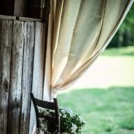 Wooden chair by a window with beige curtains, overlooking a green lawn and bright outdoor light