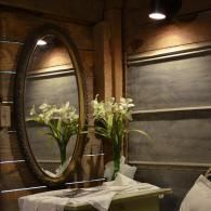 Oval mirror above a table with white lilies, in a warmly lit wood-paneled room
