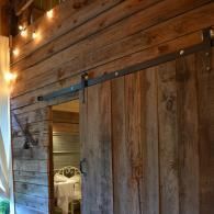 Rustic wooden barn door on a barn interior with warm string lights and an open doorway.