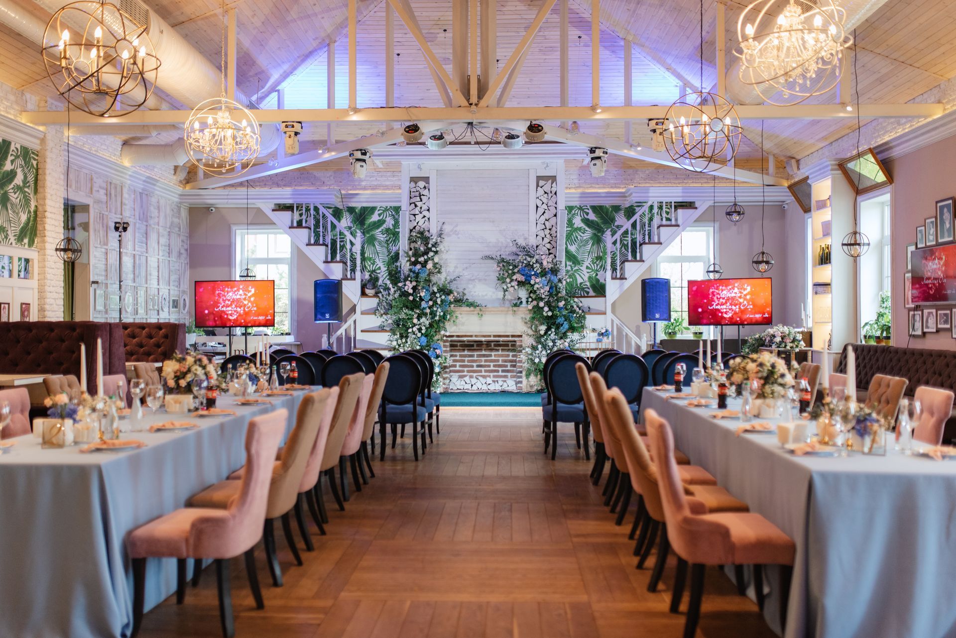 Elegant event space with long tables, chairs, stage, and decorative floral arrangements.
