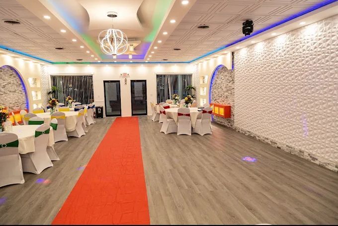 Interior of an event hall, tables with white covers, red carpet, and textured white wall.
