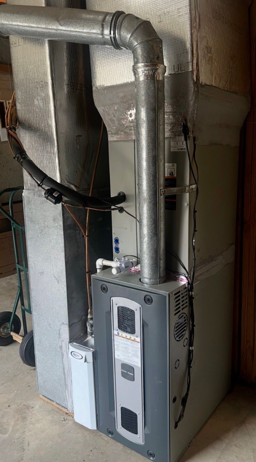 Furnace unit with silver ductwork and pipes in a basement utility area