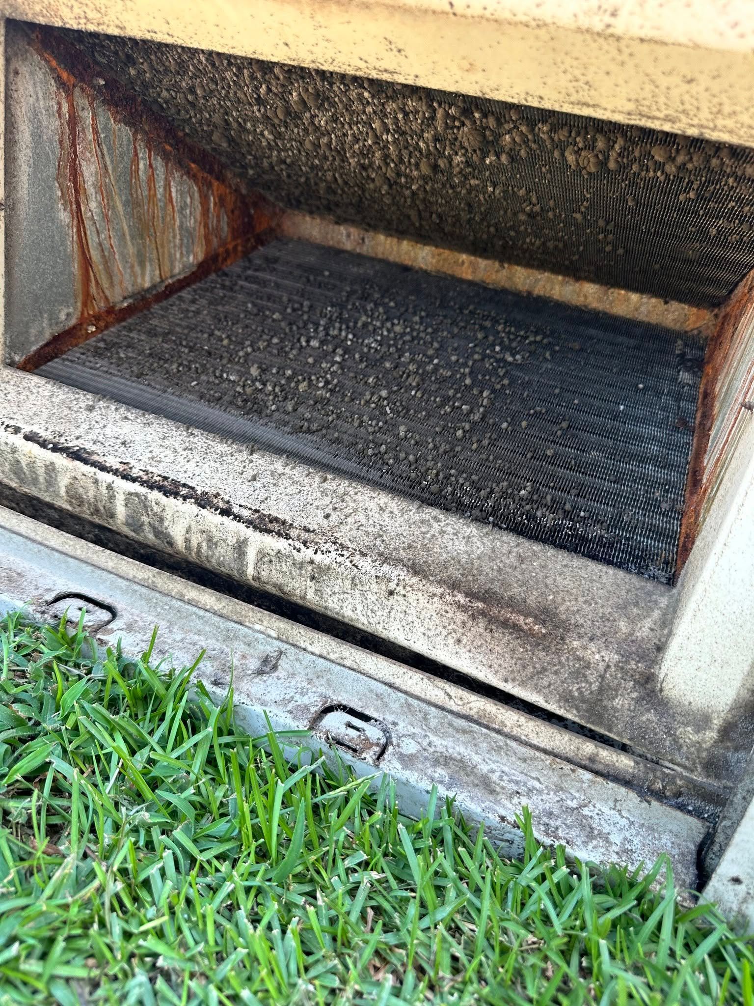 Rusty metal crawlspace vent opening above grass near a house foundation