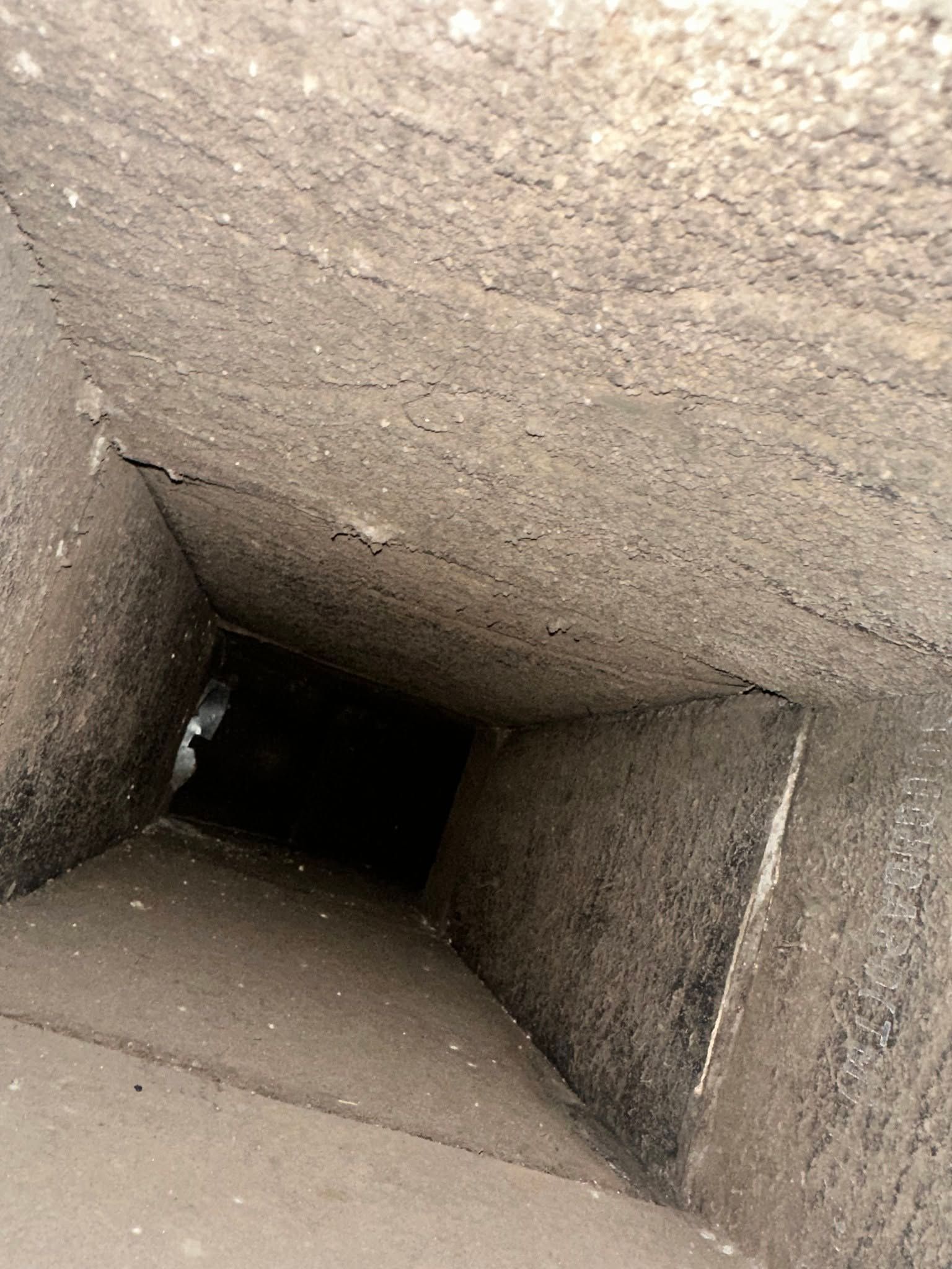 Looking down a narrow concrete shaft with a dark opening at the bottom
