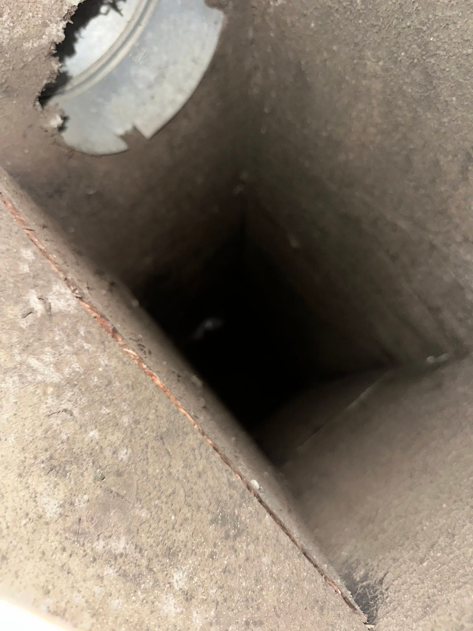 Close-up of a dark rectangular hole in a concrete surface with a metal fitting at the top left