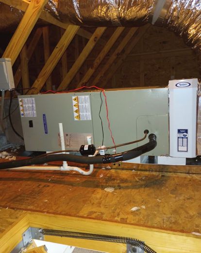 HVAC unit installed in an attic with exposed ductwork and wooden rafters