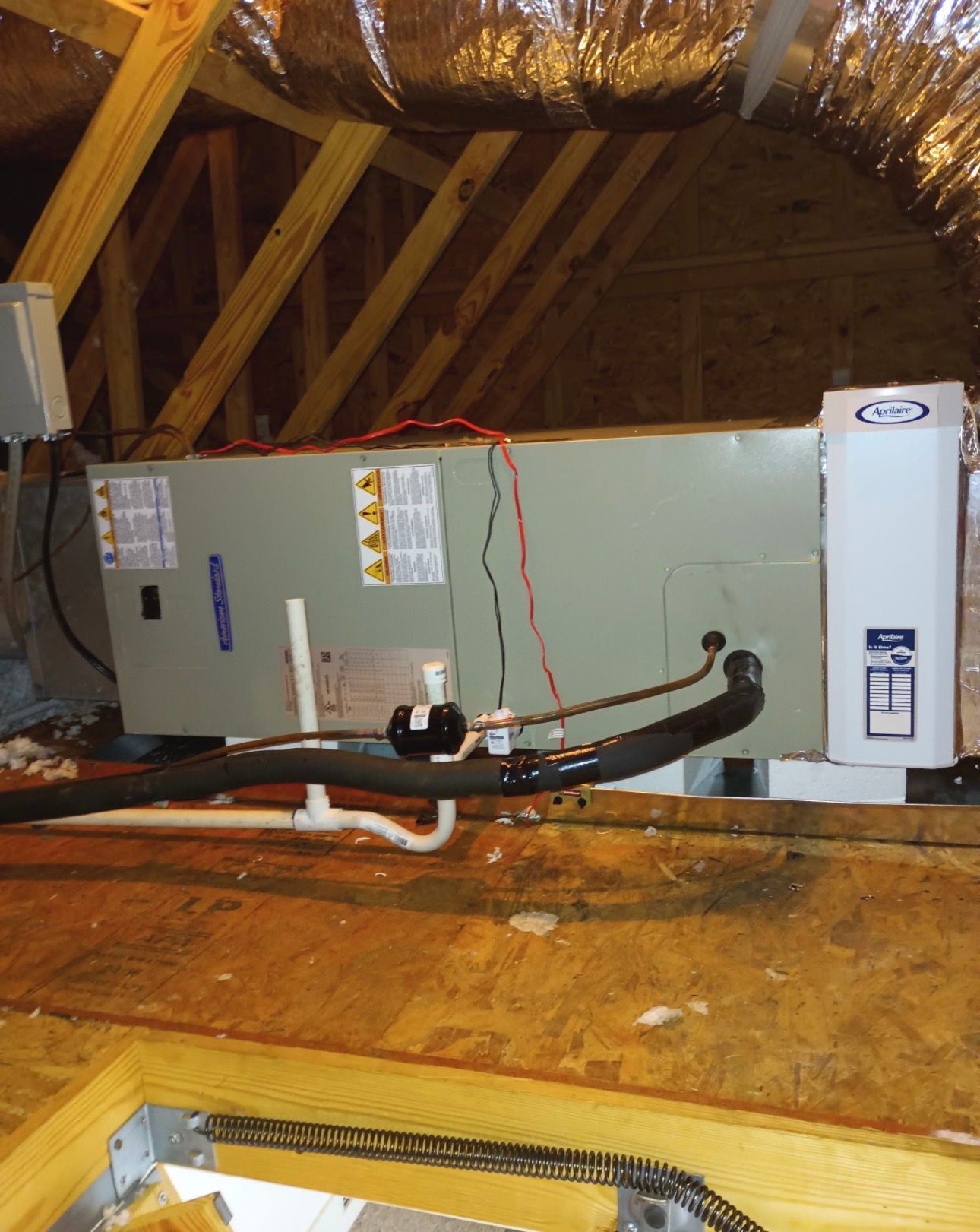 Attic HVAC unit with ductwork and insulation above a wooden floor