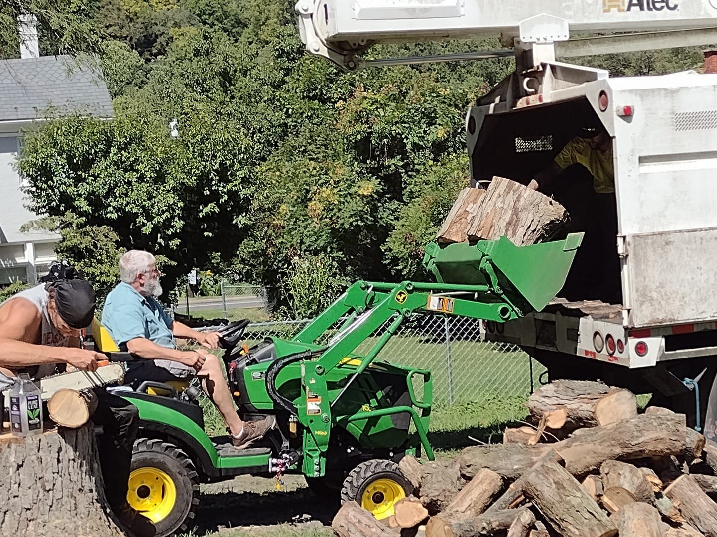 A man is sitting on a tractor next to a pile of logs.