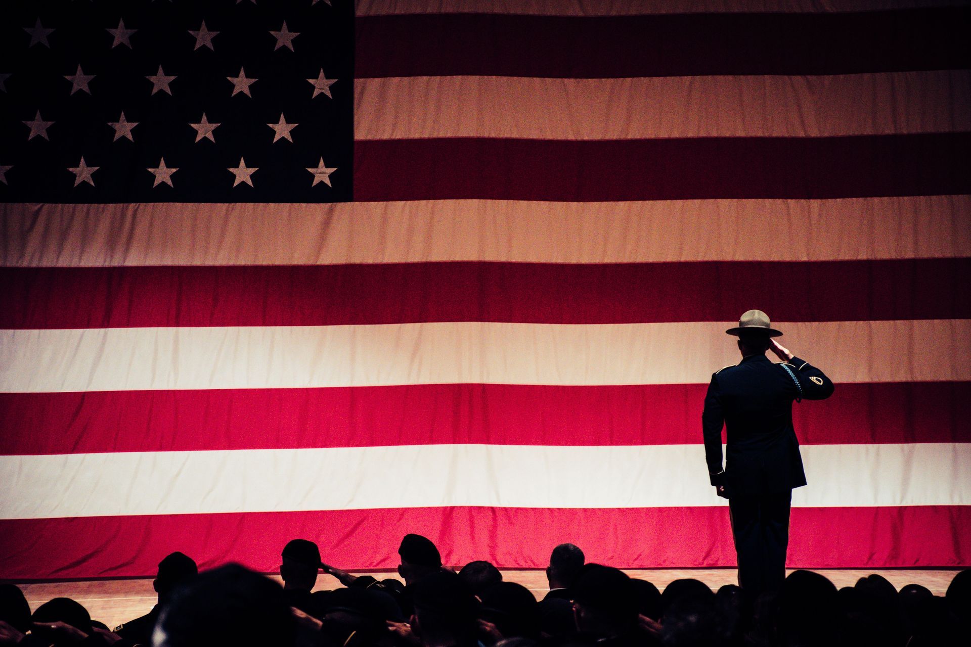 Silhouetted audience and saluting figure before a large American flag backdrop