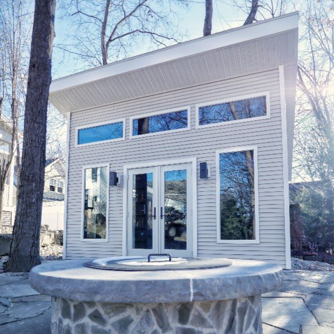 Small modern pavilion with glass doors and stone counter in a wooded outdoor setting