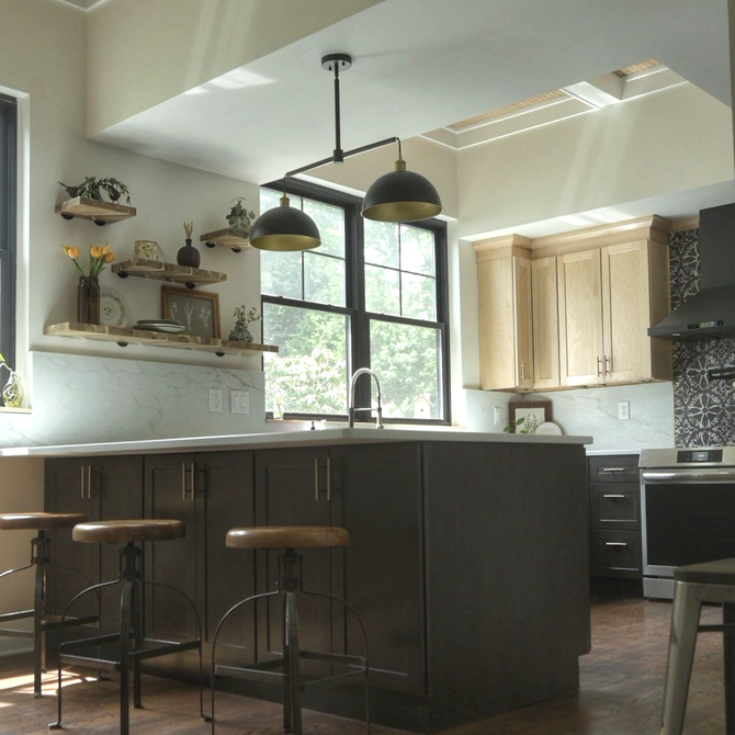 Modern kitchen with dark island, bar stools, pendant lights, and sunlight through a window.