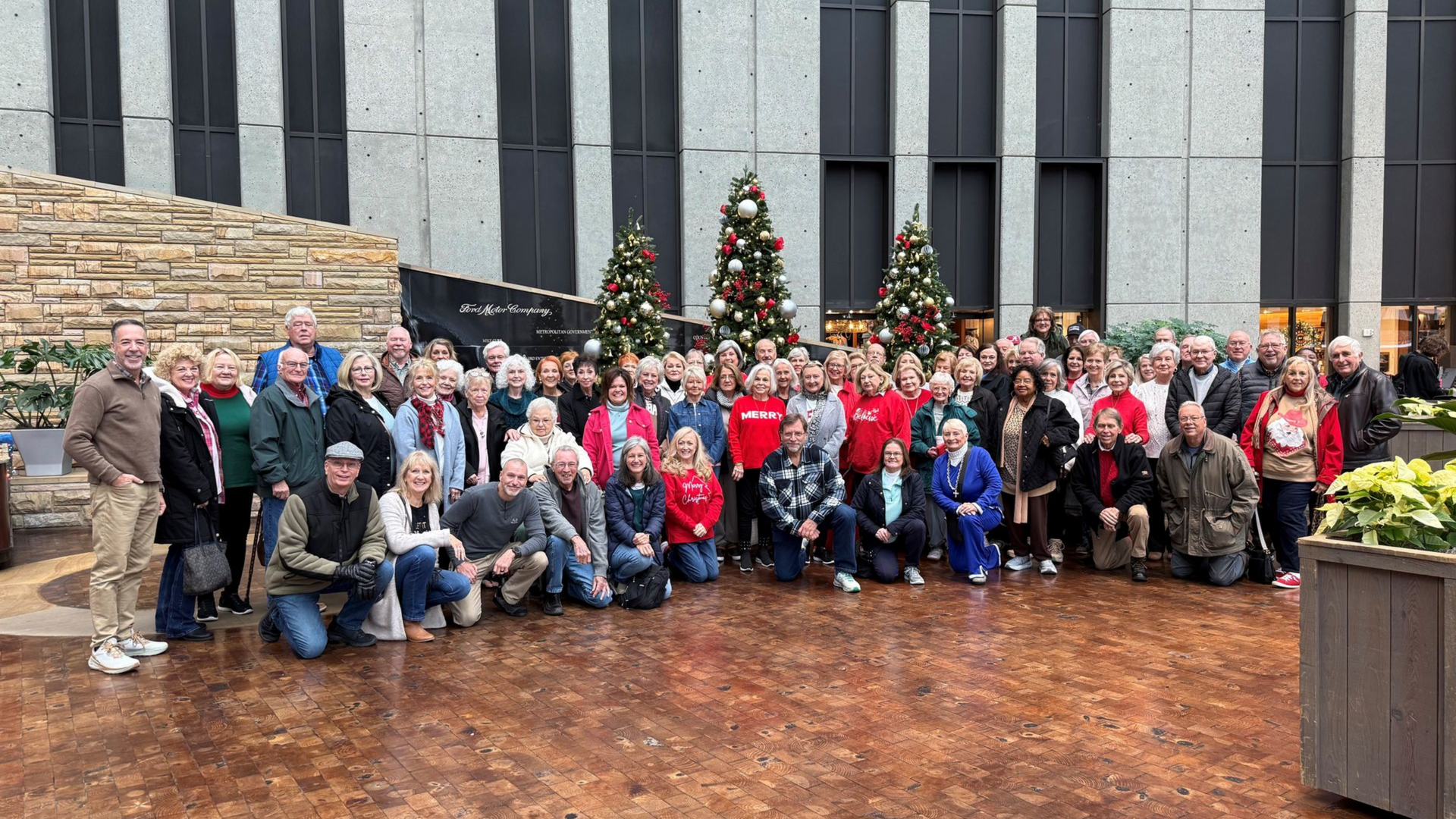 Large group posing outdoors in front of decorated Christmas trees and a stone building