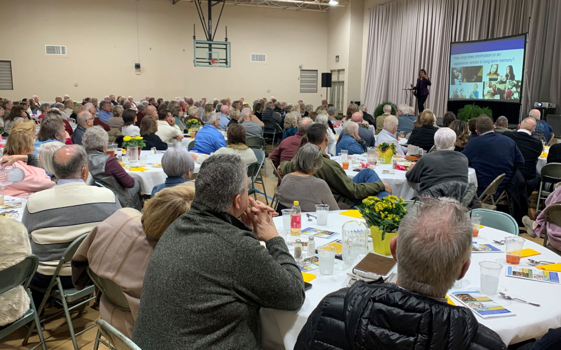 Community meeting with a large seated audience watching a presentation on a screen in a hall