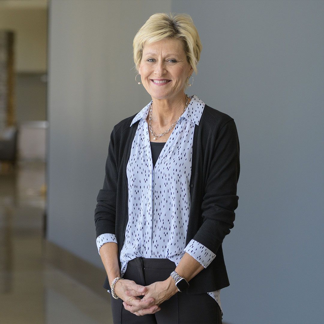 Smiling woman standing indoors in a black cardigan and patterned blouse