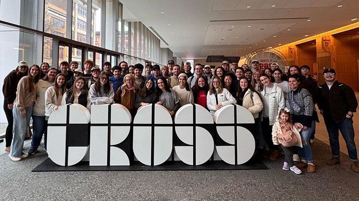 Group posing indoors behind a large “CROSS” sign.