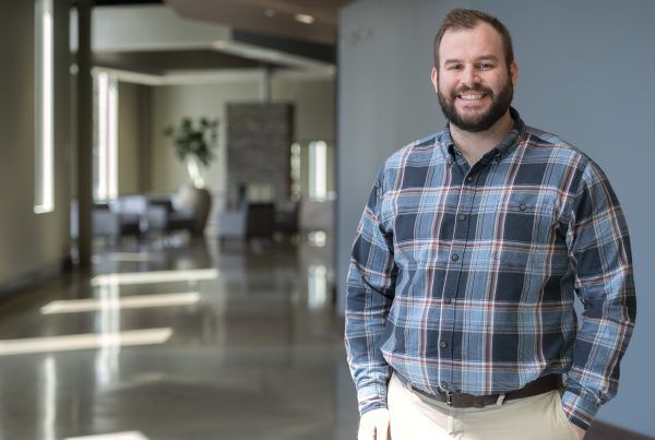 Smiling man in a blue plaid shirt standing in a modern office lobby