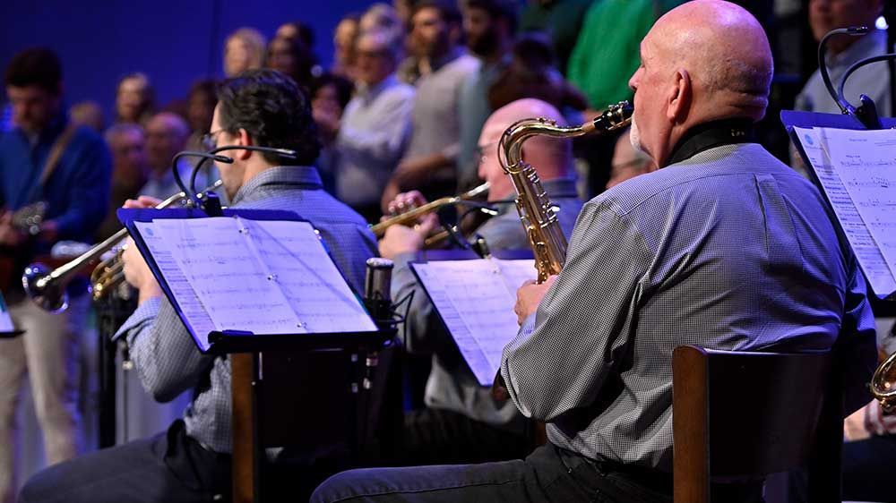 Musicians seated on stage playing saxophones with sheet music stands in a concert setting
