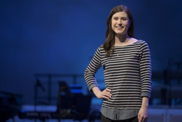 Woman in a striped shirt smiling on a stage with a blue-lit background