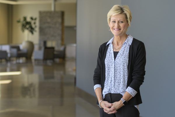 Woman standing in a modern office lobby, smiling with hands clasped