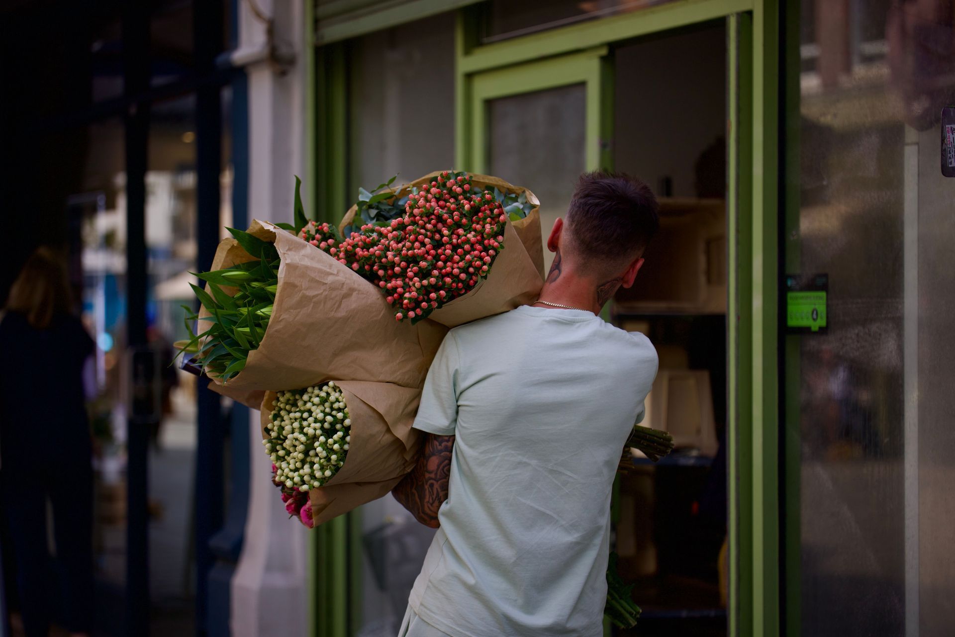 Person carrying large bouquets of flowers into a storefront entrance