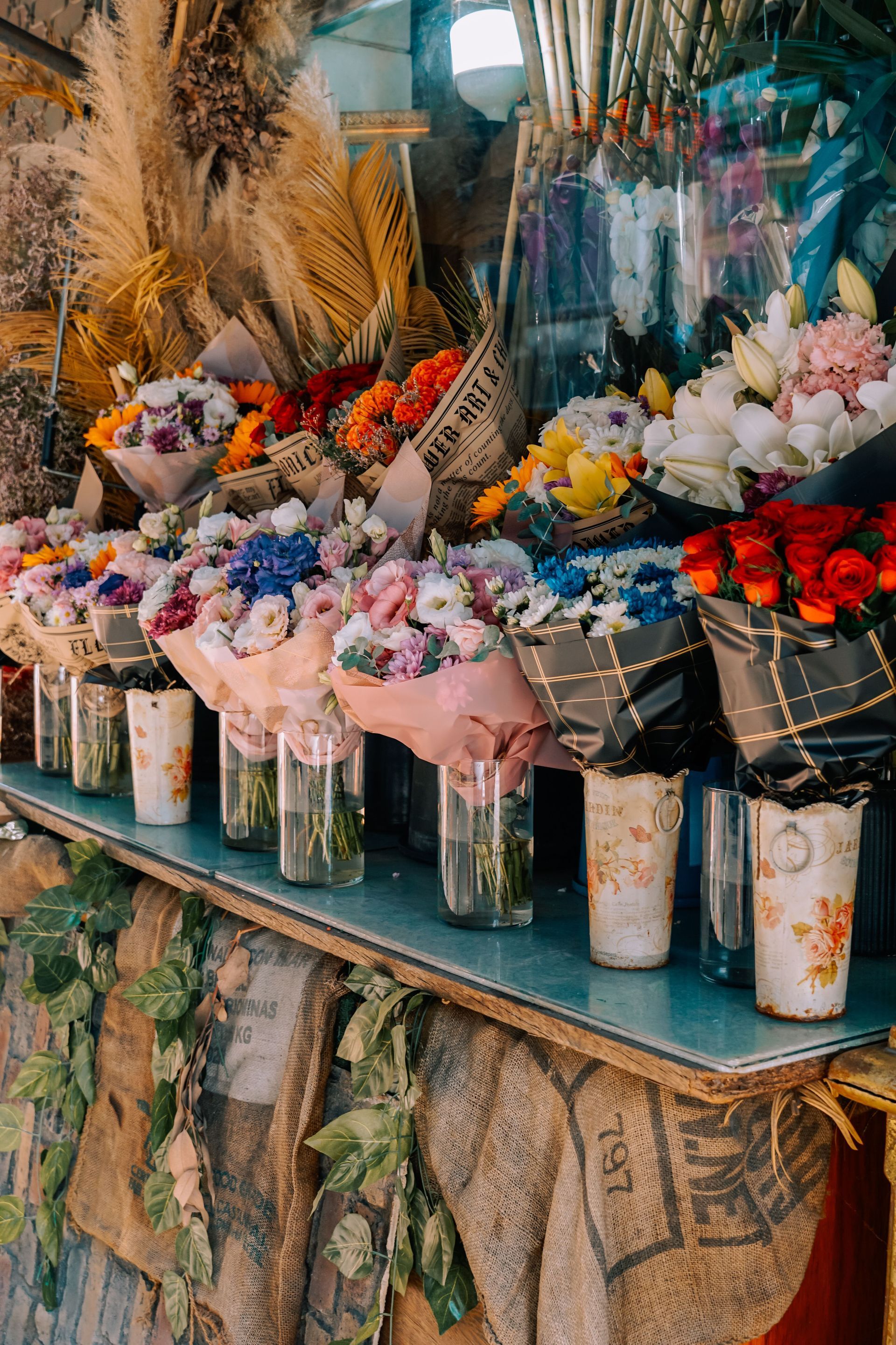 Bouquets of colorful flowers in glass jars at a market stall, with dried grasses and greenery behind them