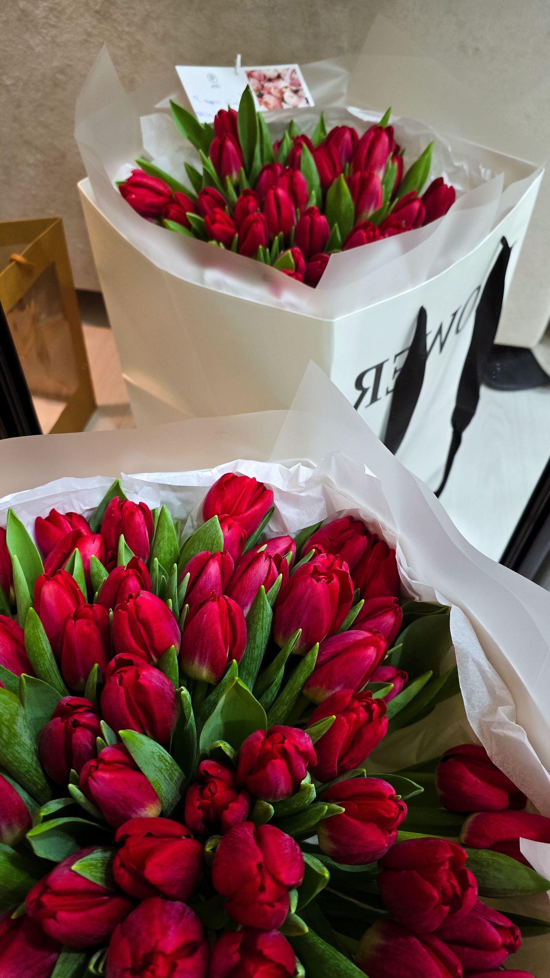 Two bouquets of red tulips wrapped in white paper on a table