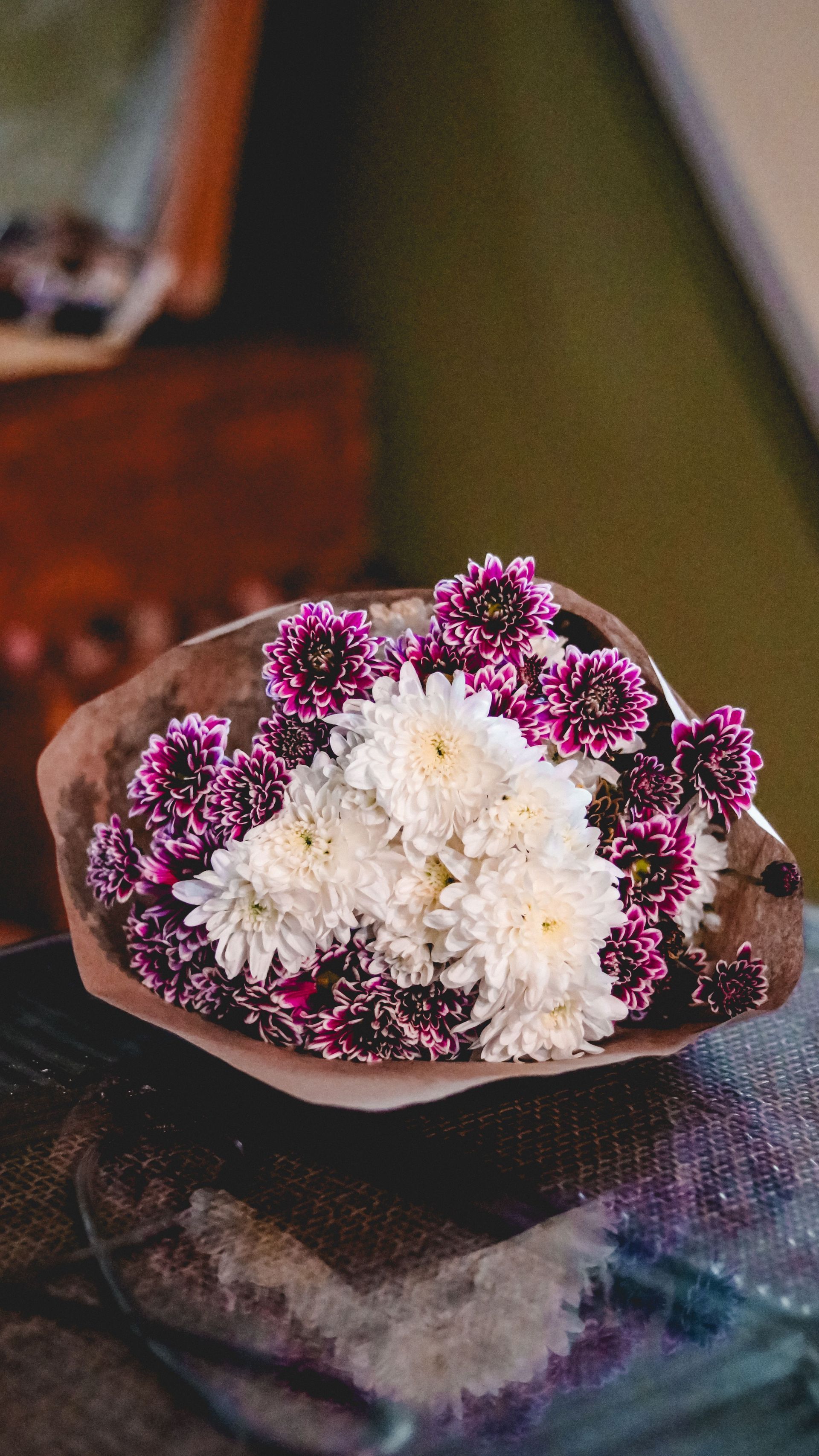 Small floral arrangement of white and purple flowers in a brown woven bowl on a reflective table