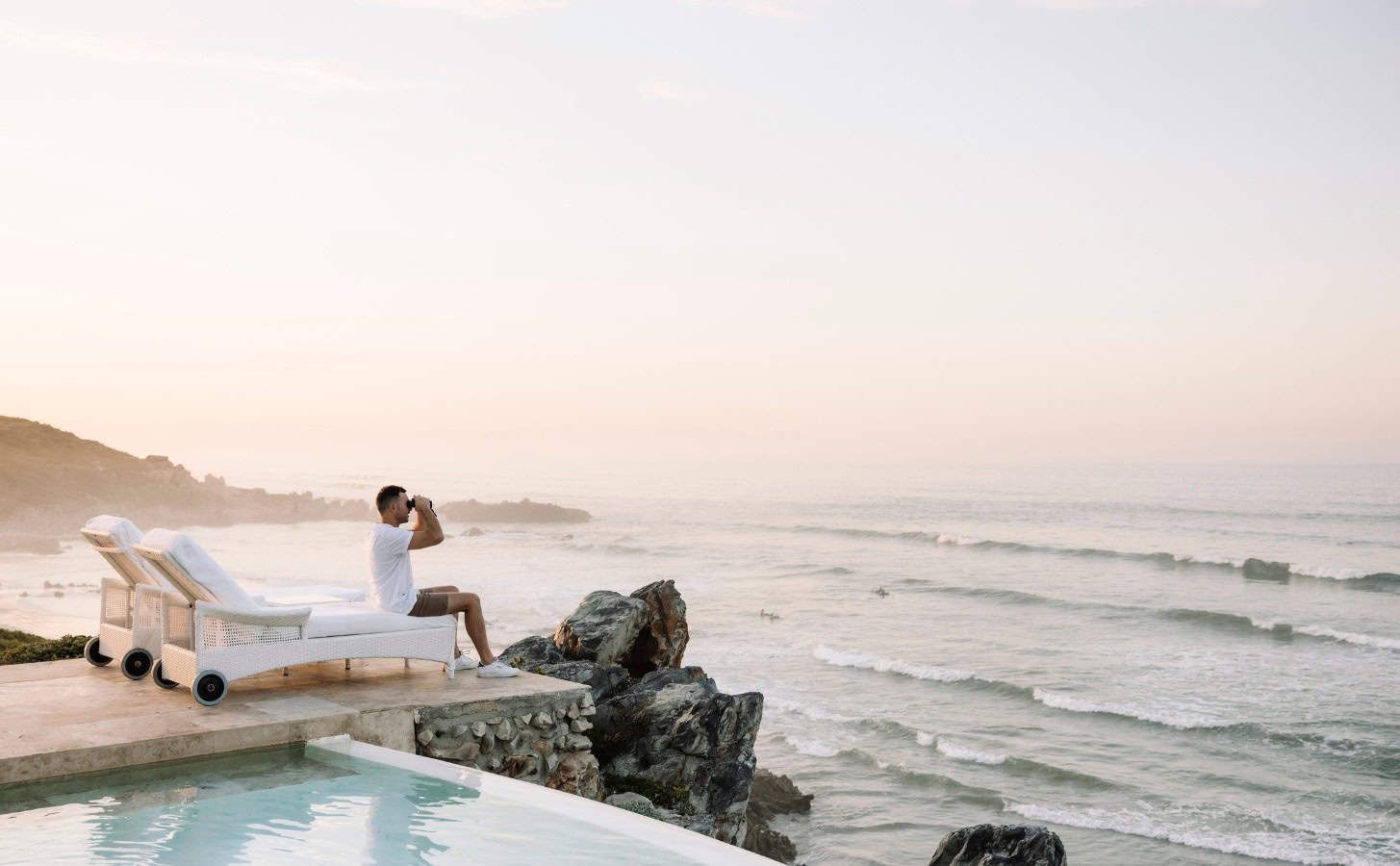 Person reclining on a poolside lounge chair overlooking a calm ocean at sunrise