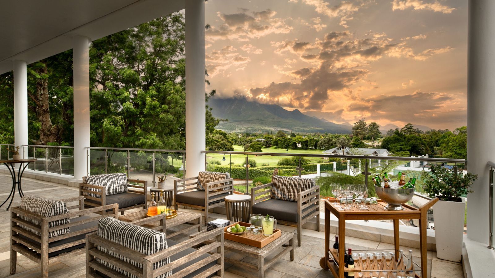 Covered patio with woven seating and table overlooking a green landscape at sunset