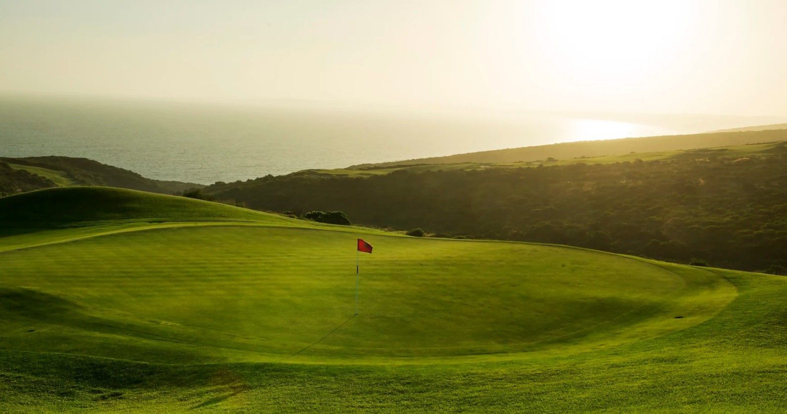 Sunlit green hillside golf course and the ocean in the distance