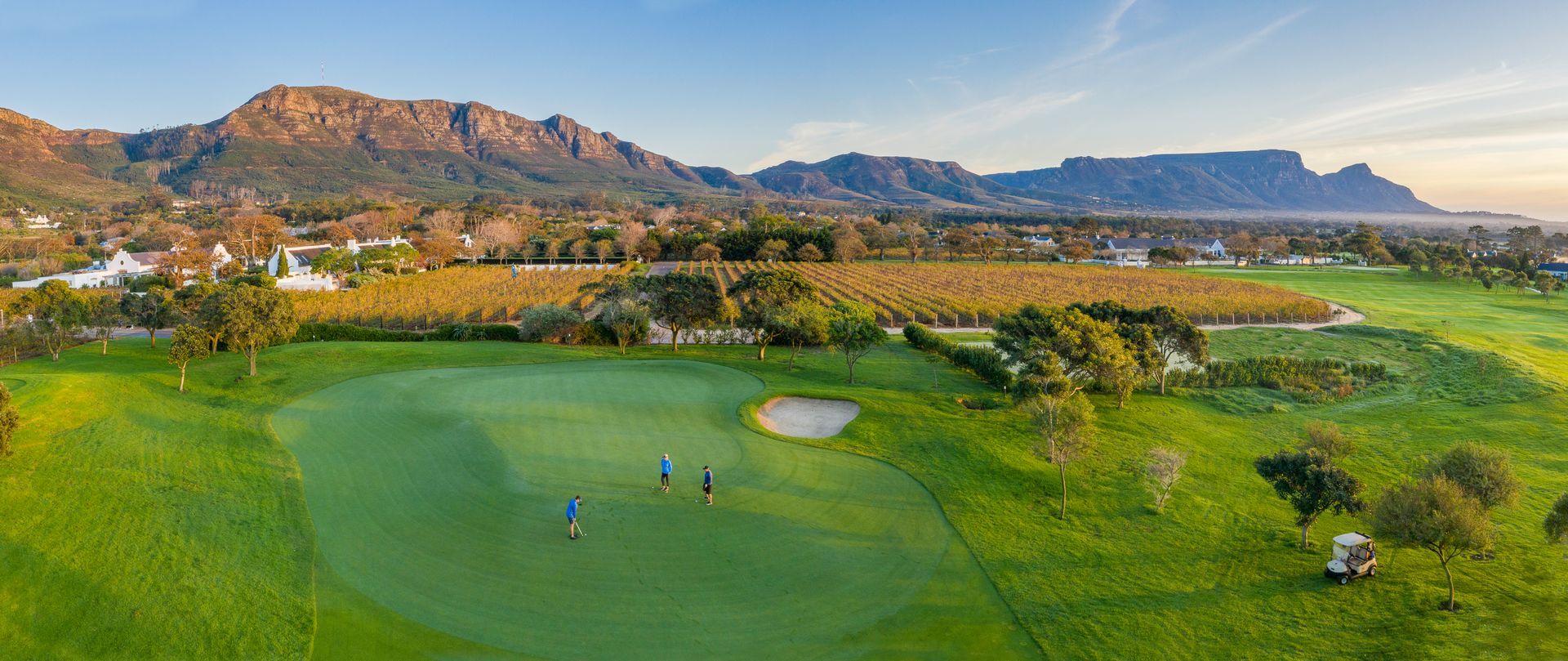 Golf course with players, green fairways, and mountains under a clear sky