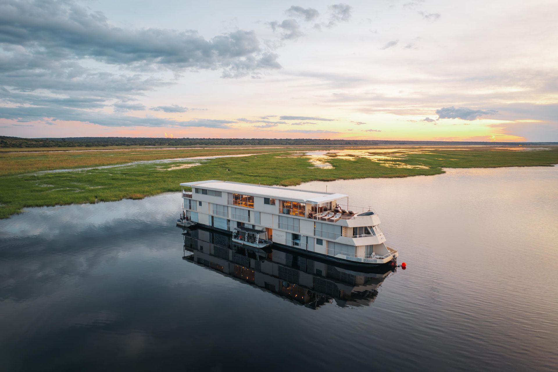 White cruise boat on calm river at sunset beside green marshland