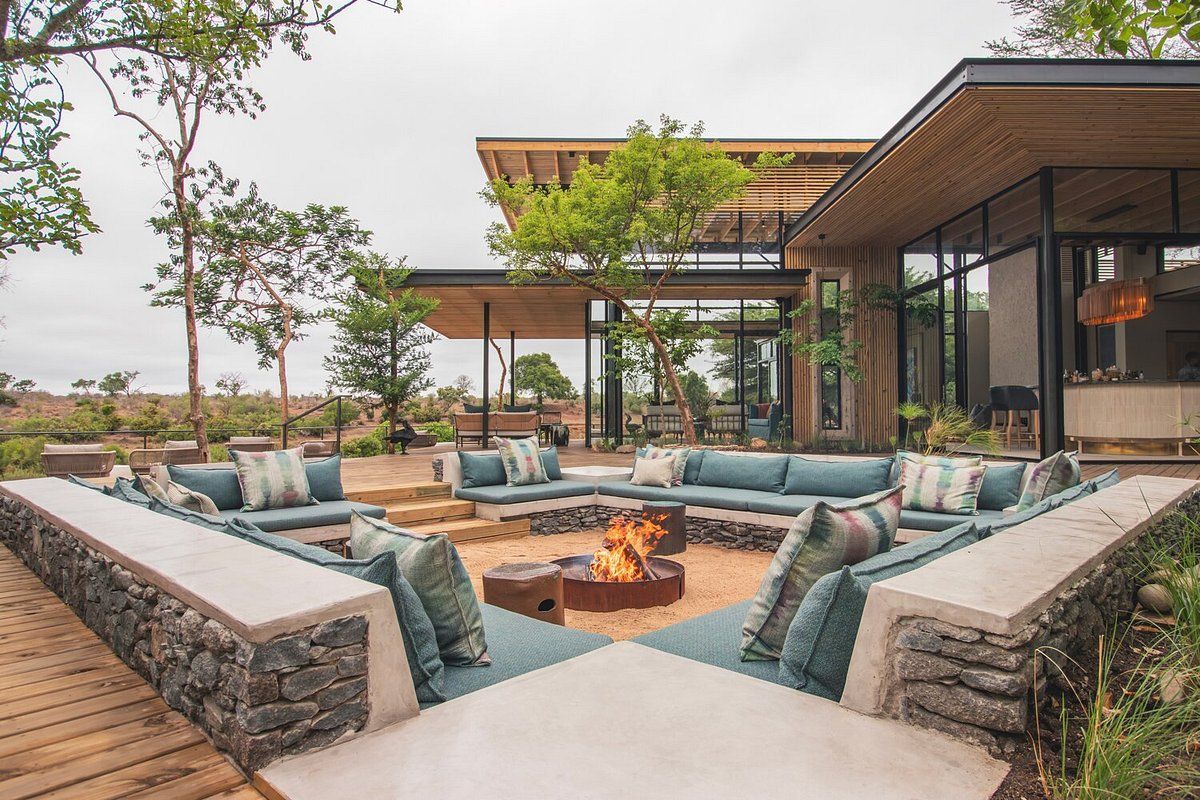 Modern outdoor patio with stone fire pit, lounge seating, and glass-walled lodge