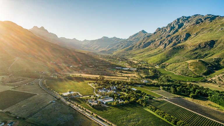 Sunlit mountain valley with green fields, a small village, and winding roads at sunrise