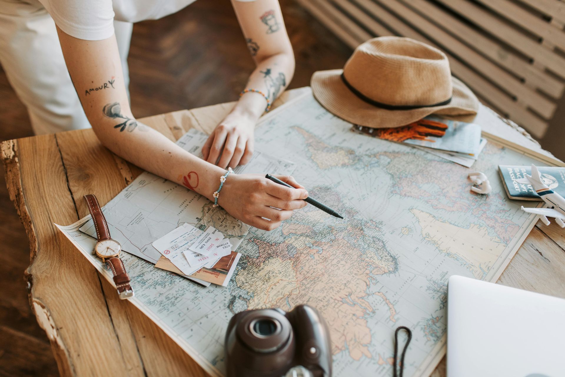 Hands marking routes on a world map beside a notebook and camera on a desk