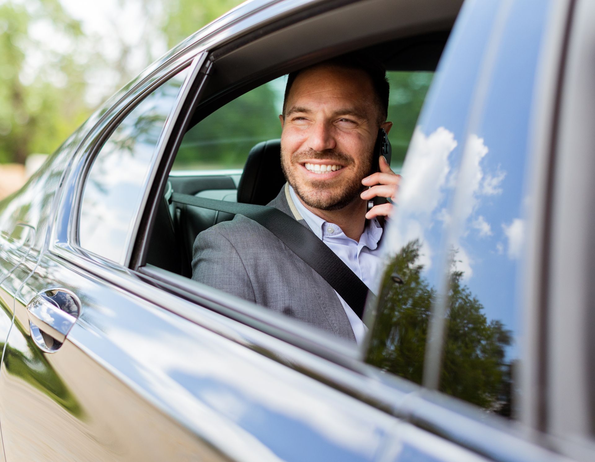 Smiling man in a car using a smartphone, seen through the open window.