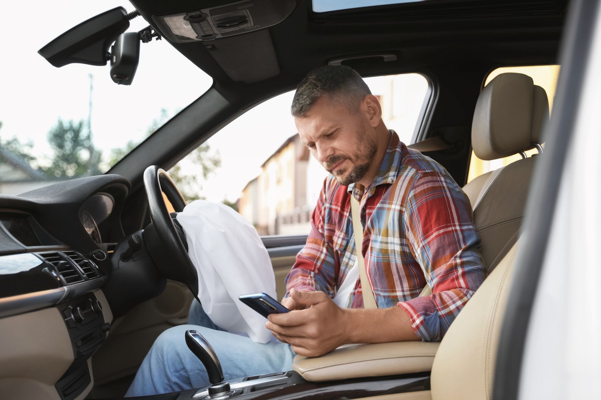 Man in a red plaid shirt using a smartphone while sitting in a car’s front passenger seat