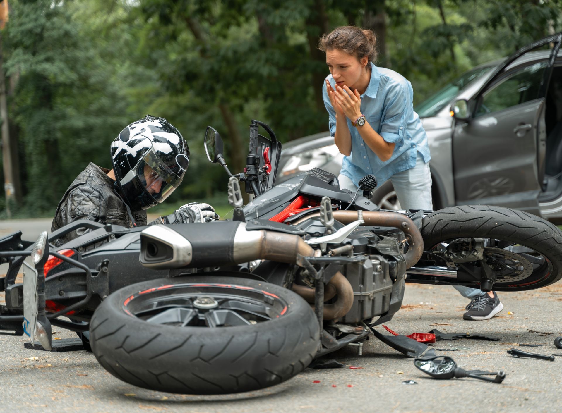 Motorcycle crash scene with overturned bike, debris on road, and a man crouching beside the wreckage