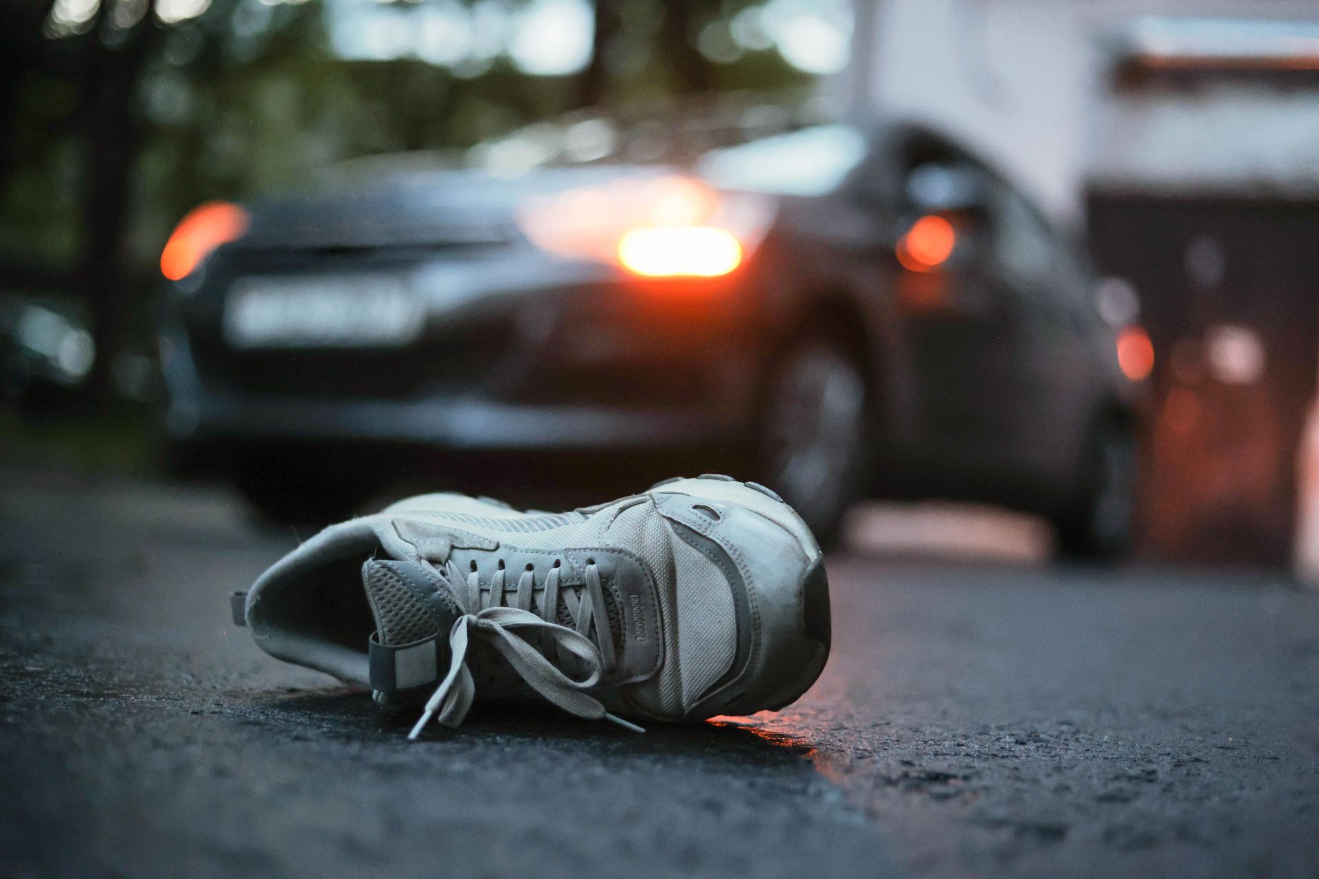 Shoe lying on wet road after a car accident, with a blurred damaged car in the background