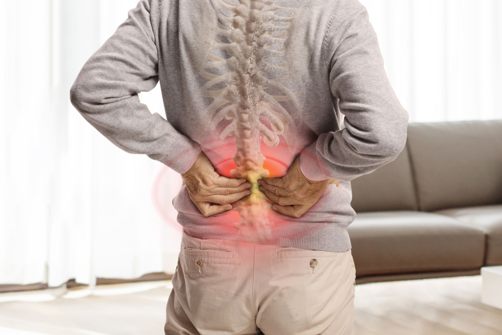 Person holding lower back with red pain highlight, standing in a living room