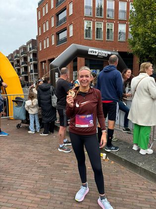 Een lachende hardloper in een bordeauxrode top en zwarte legging staat samen met andere deelnemers aan de startlijn van een stadsloop.
