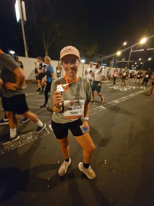 Een hardloper lacht bij de finishlijn van een nachtelijke race en houdt een medaille omhoog voor de straatlantaarns.