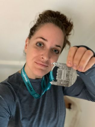 Persoon die een medaile  omhoog houdt, gekleed in een blauw shirt en met een keycord om, binnen.
