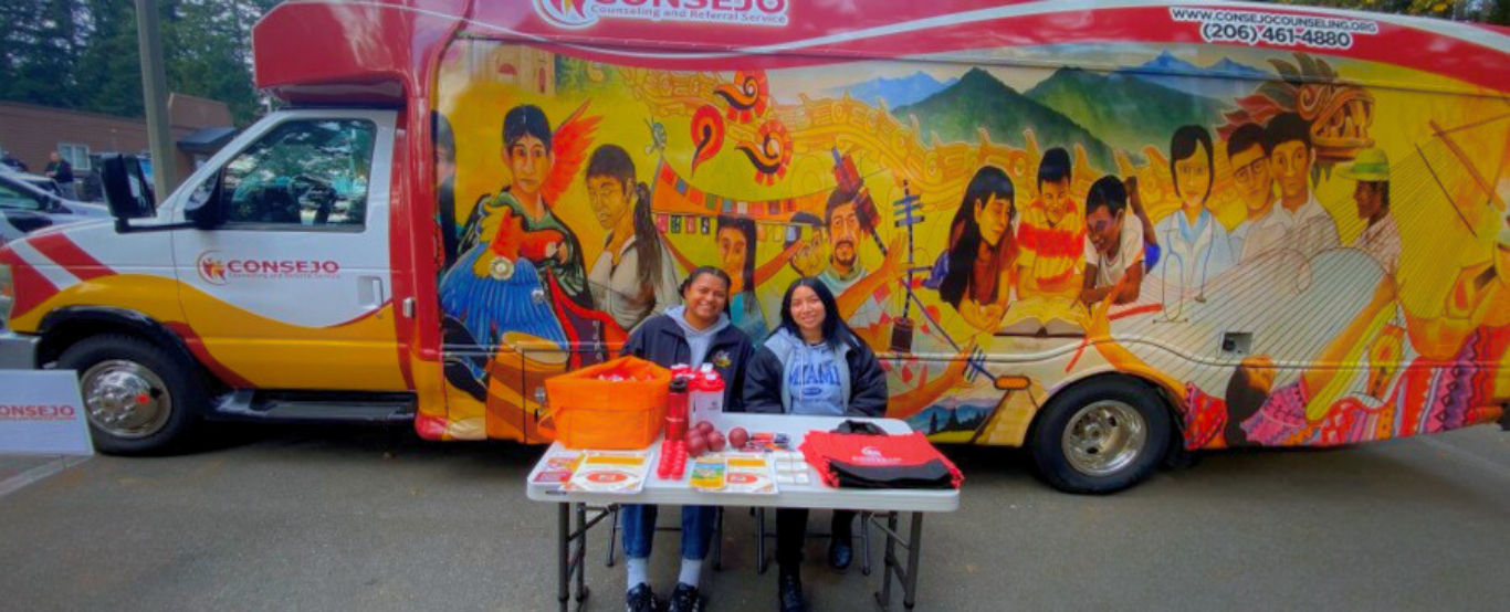 A group of people are sitting at a table in front of a truck.