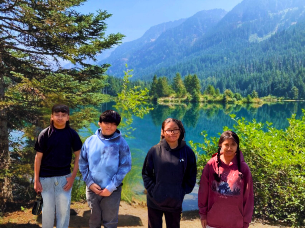 A group of people standing in front of a lake with mountains in the background.