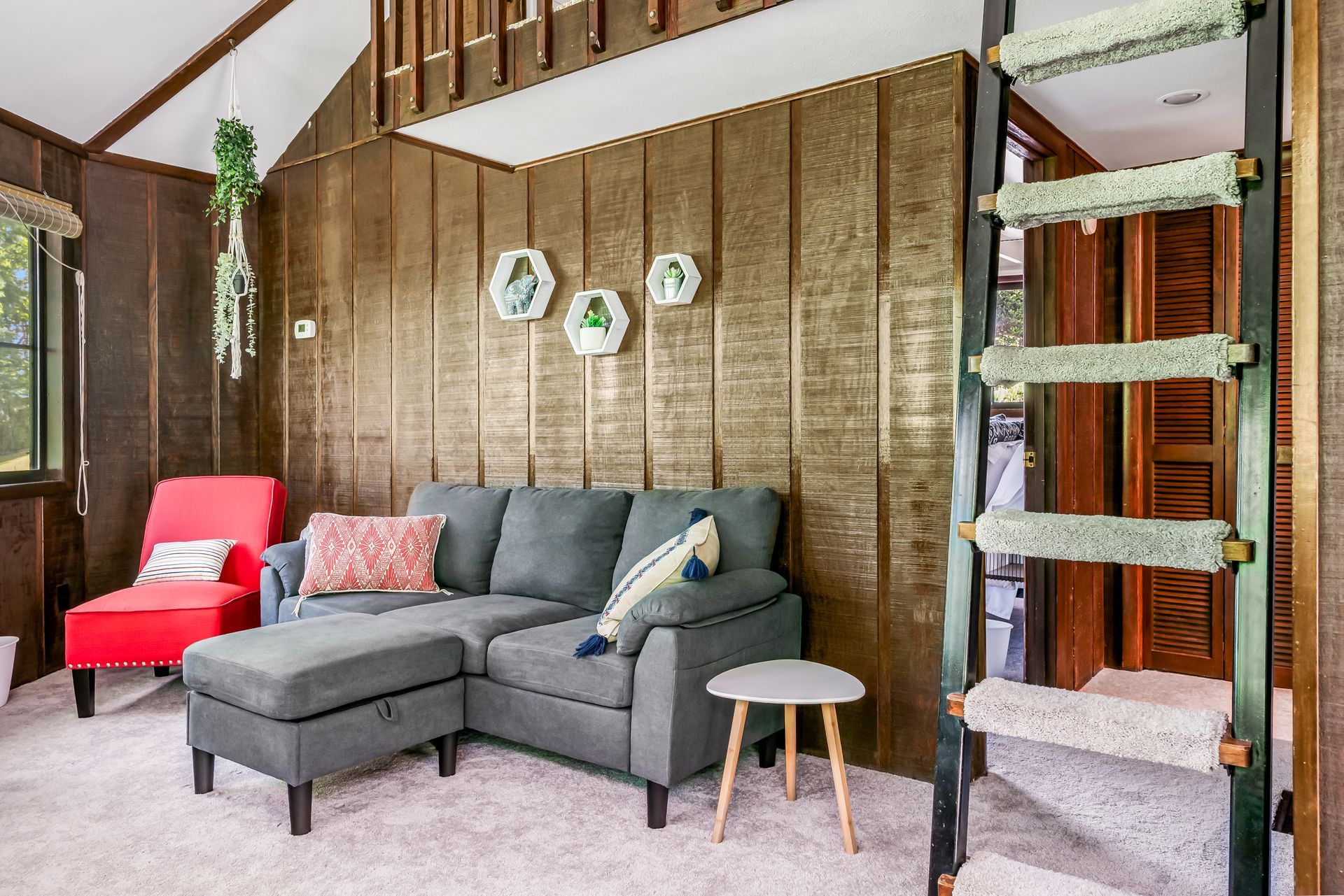 Cozy cabin living room with sectional sofa, red chair, and a ladder to a loft. Gold wood paneling.